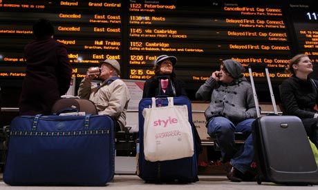 Passengers sit underneath an electronic train schedule