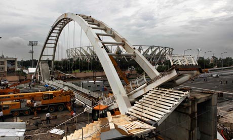 Indian workers stand at the scene of bridge collapse near Jawaharlal Nehru stadium in New Delhi