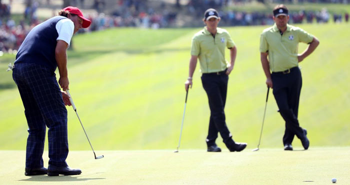 Graeme McDowell and Rory McIlroy look on as Phil Mickelson of the USA putts on the 4t