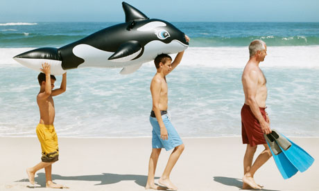 Boys on beach carrying dolphin inflatable