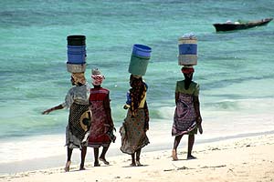 2 Women carry buckets on their heads as they walk the beach route on their way to work in Nungwi, Zanzibar