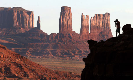 A photographer stands on an overlook as he takes a photograph of Monument Valley.