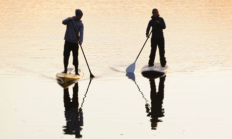 Two people rowing paddle boards in water at dusk