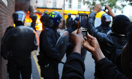 Onlookers film and photograph a burning car during the riots in London