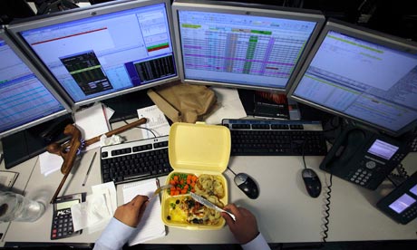 A dealer eats his lunch as he monitors his screens on the trading floor of IG Index in London