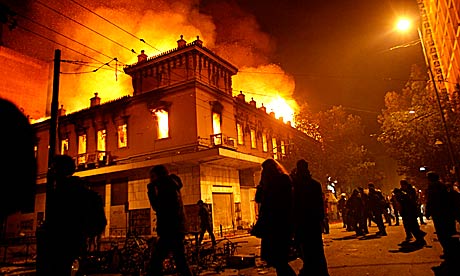 Protesters pass by a burning cinema in Athens