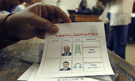 An Egyptian electoral official holds a ballot paper as a woman arrives to cast her vote