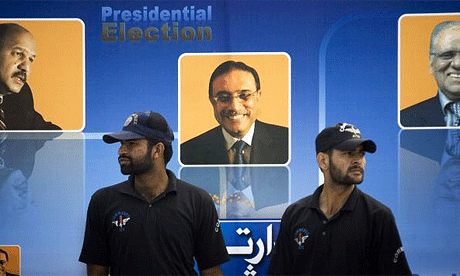 Pakistani security forces stand next to posters of the presidential candidates, including Asif Ali Zardari, centre