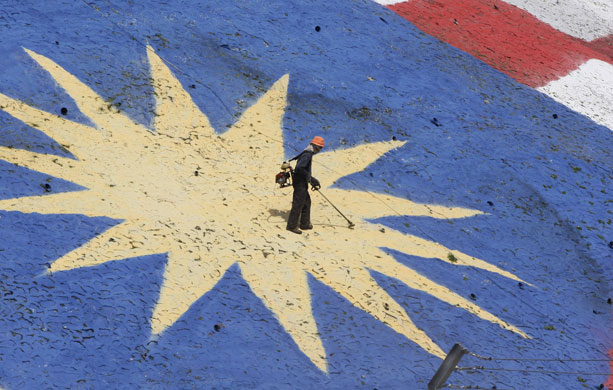 Sport: 24 hours: A worker cuts the grass printed with a giant Malaysian flag 