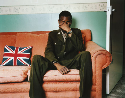 Isolation: A young black solider in uniform sits at home coveing his face