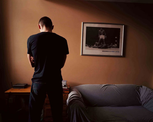 Isolation: A war veteran stands alone in a hostel, his back to the camera