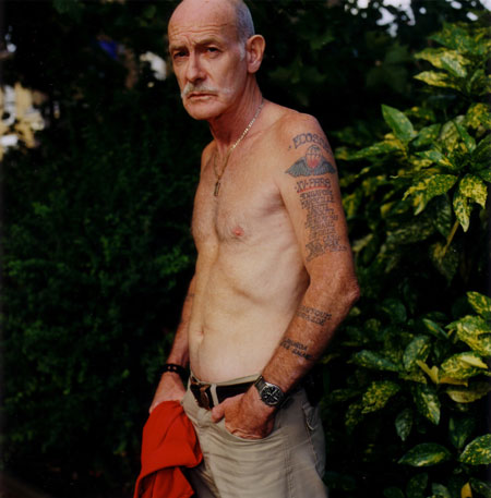 Isolation: A veteran stands outside, shirtless, showing an arm full of tattoos