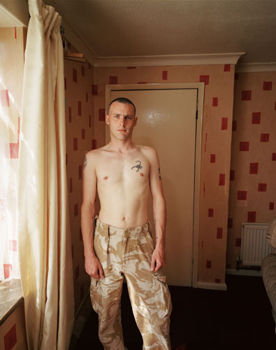 Isolation: A man stands near a window in army trousers, no shirt