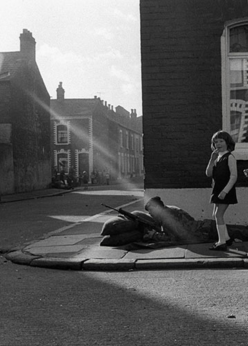 A girl stands next to a soldier on a Derry street