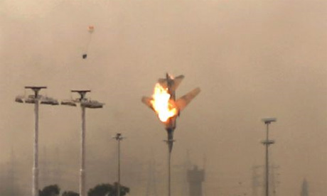 A burning jet plunges to the ground in Benghazi, Libya, with a pilot's ejection seat and parachute apparently visible in the background