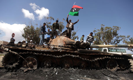 Libyan rebels wave their flag on top of a wrecked tank belonging to Gaddafi's forces in Benghazi