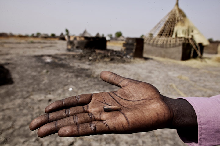 Africa Unrest: A survivor displays a bullet in front of burnt houses in Sudan
