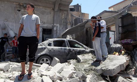 Libyan youths stand on rubble of a house burying a destroyed car in Tripoli