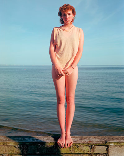 Joel Meyerowitz Monograph: A red-headed girl stands full length with sea behind