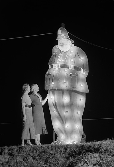 Blackpool illuminations: 1936:  Two holidaymakers by a large illuminated policeman at Blackpool