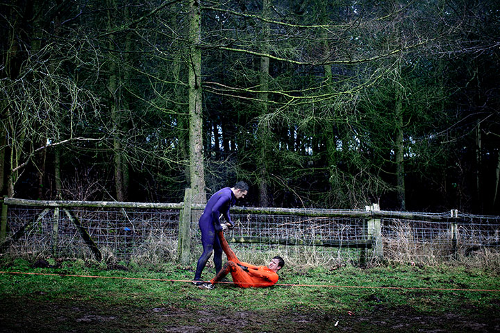 Tough Guy - Weekend: Man in blue helping another man in red with cramp in forest