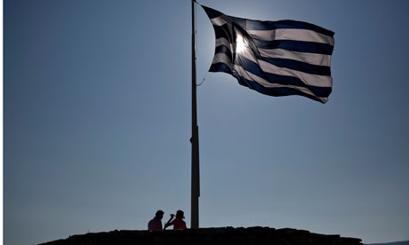 Tourists rest beneath a Greek flag atop the hill of the Acropolis in Athens