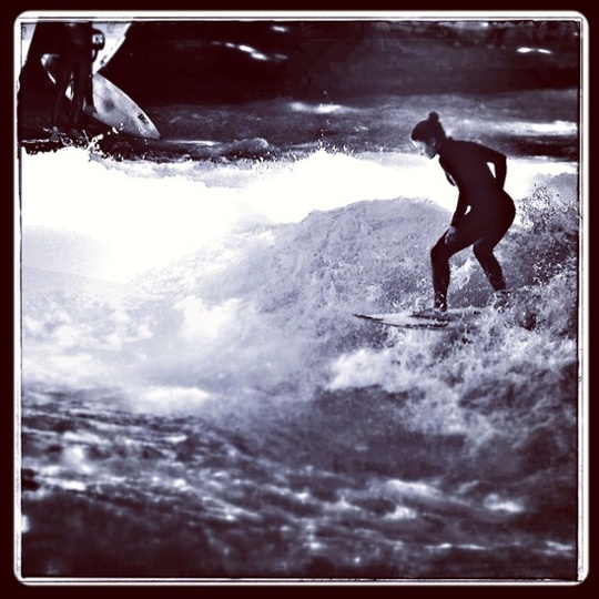 Young woman surfs on a permanent wave on the famous Eisbach river in Munich