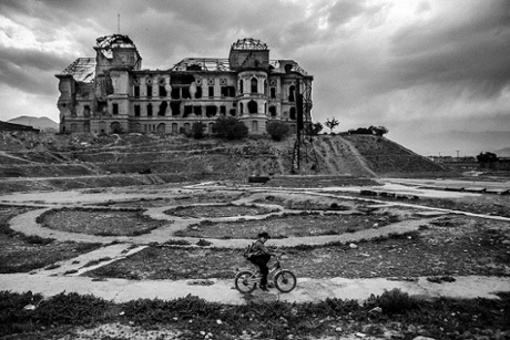 A student cycles past the ruins of a palace destroyed by the conflict
