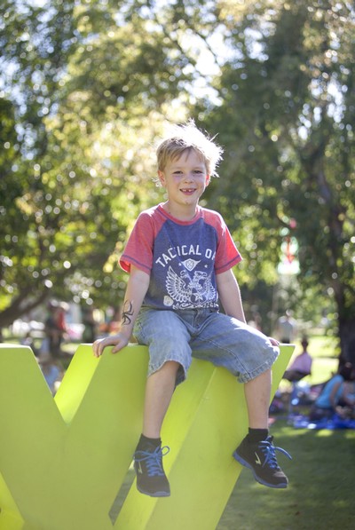 WOMADdelaide festival: Hugo, 6, from Adelaide sits on the WOMAD sign