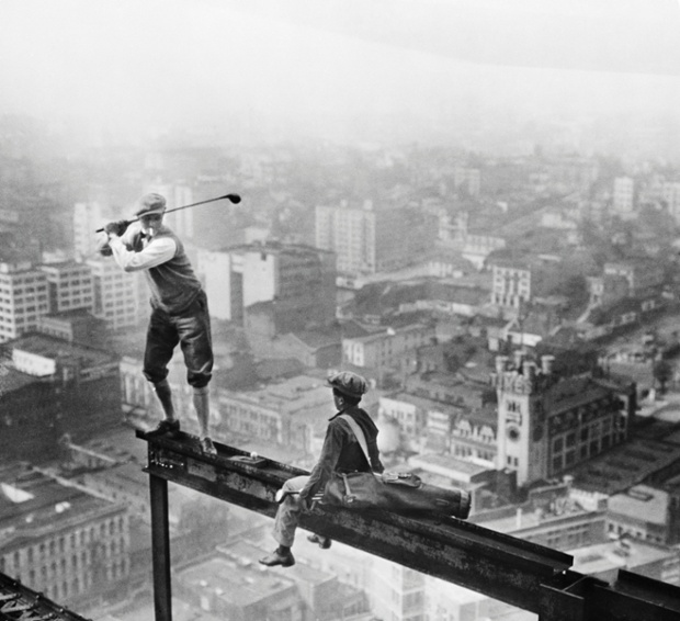 A cigarette smoking golfer and his caddy teeing off on the girder of a building under construction in Los Angeles in 1927.