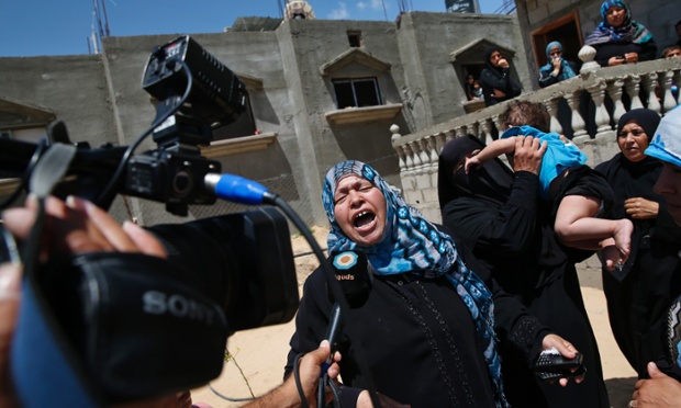 A Palestinian mourner cries as she talks to a TV  journalist, while the bodies of Mousa Abu Muamer, 56, and his son Saddam, 27, who were killed in an Israeli missile strike at their house are brought in during their funeral procession, on the outskirts of the town of Khan Younis, southern Gaza Strip.