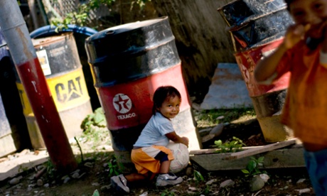 A child from the Huaorani tribe, also known as the Waos, who are native Amerindians from the Amazonian Region of Ecuador, plays near a discarded Texaco oil drum